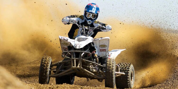 Cuatrimoto, con pilototo con casco en playa, con arena